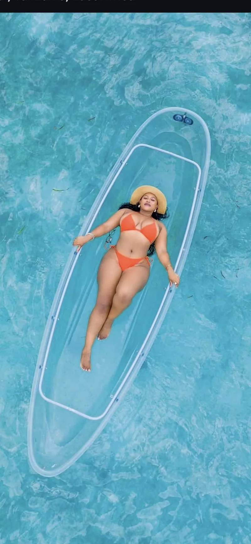 A woman sunbathing in a glass-bottom kayak off the Zanzibar coast